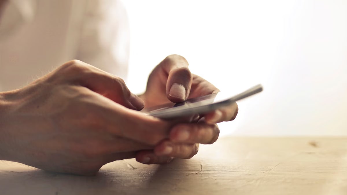 Close-up of an individual's hands holding a smartphone on a table indoors.